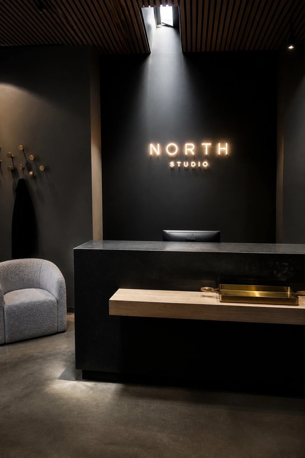 A modern reception desk in dark stone with a light wood ledge in front, set against a black wall with an illuminated sign above.