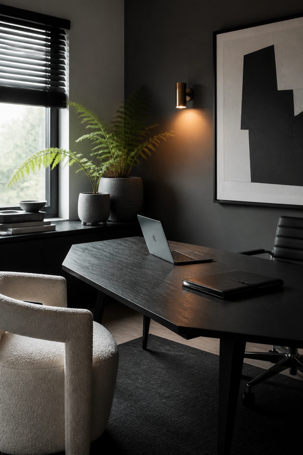 A modern office interior featuring a dark wood desk with a laptop and notebook, a white bouclé chair in the foreground, a black office chair, potted ferns near a window with blinds, and abstract black and white artwork on a dark gray wall.