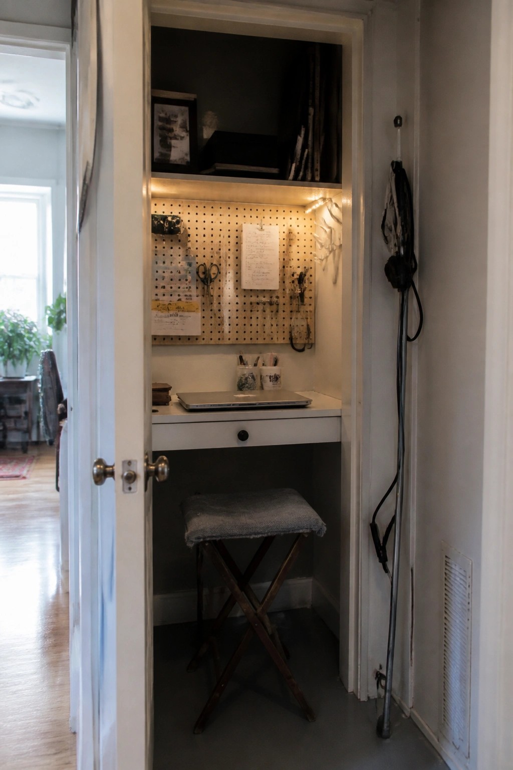 A closet converted into a small home office with a white desk, wooden folding stool, and pegboard wall.