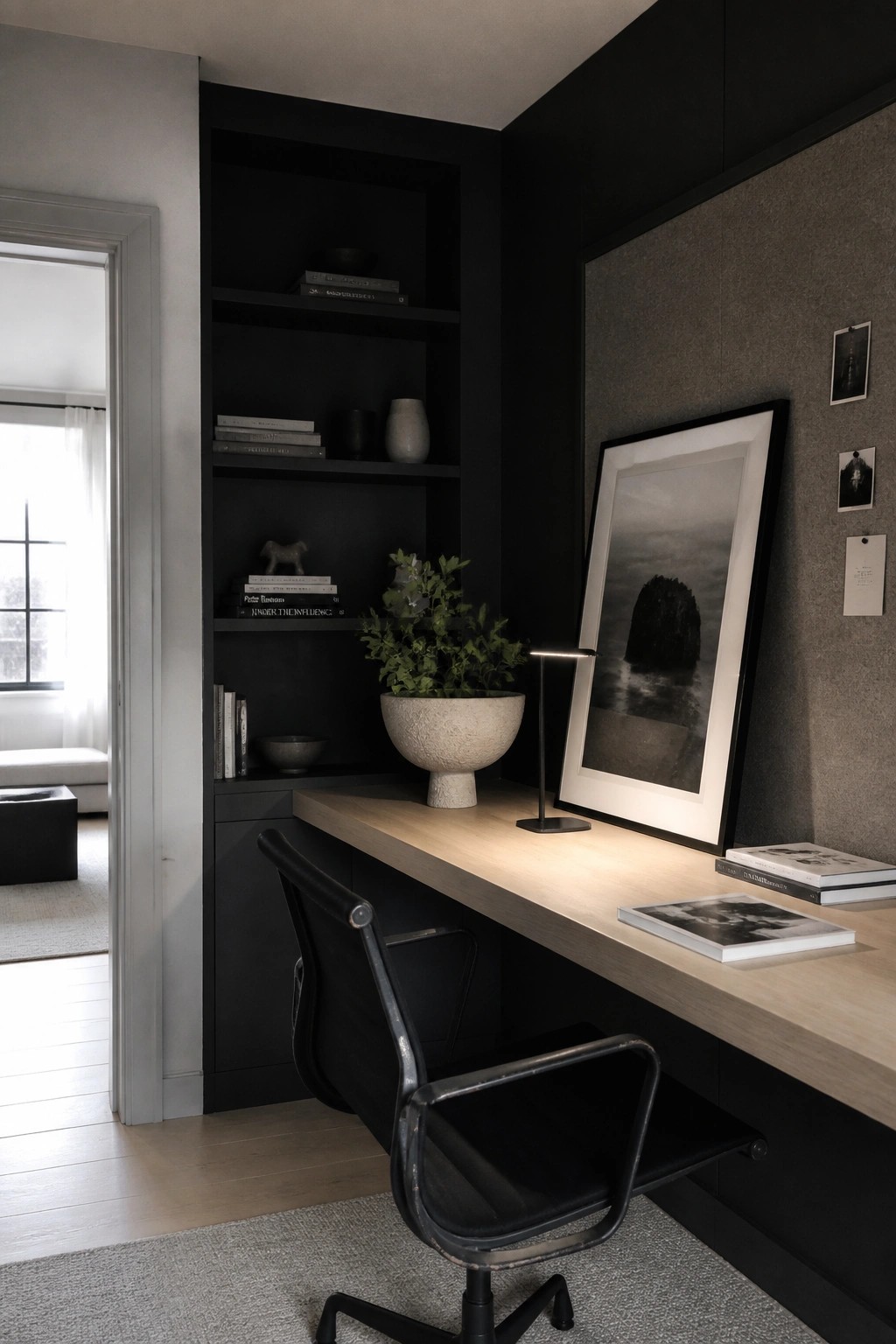 Modern minimalist office with black shelves, light wood desk, black chair, and framed art.
