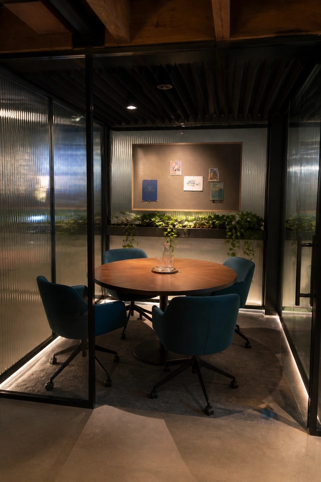 Circular wooden table with four teal chairs in glass-walled modern meeting room