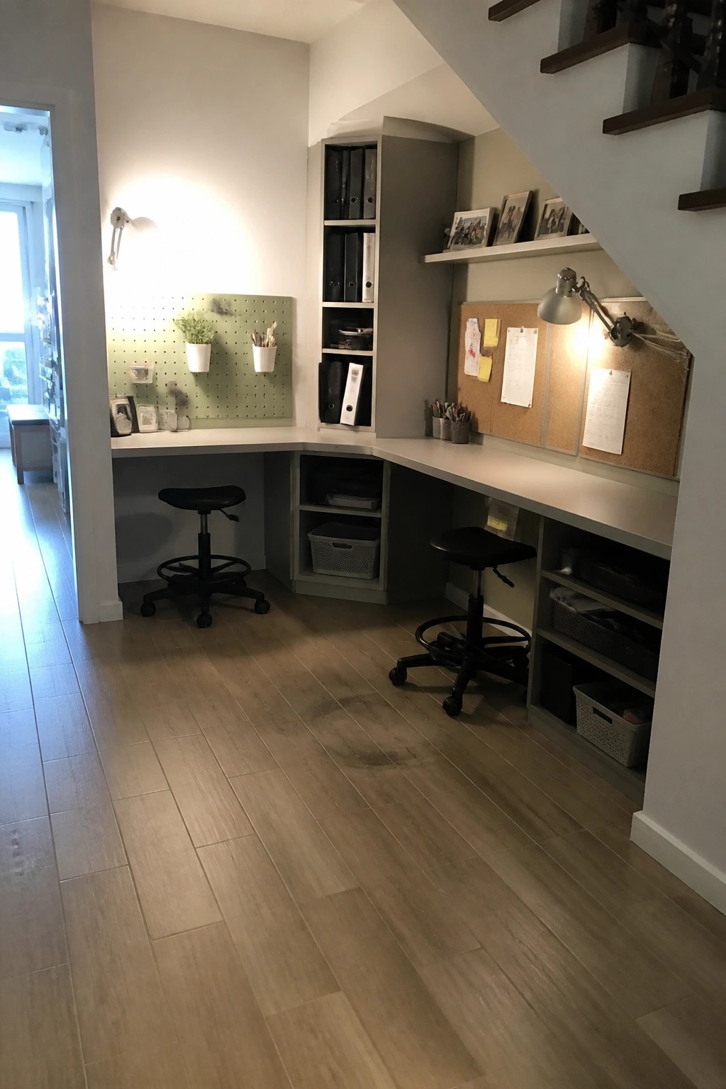 Built-in L-shaped desk under stairs with black stools, pegboard, corkboard and storage shelves