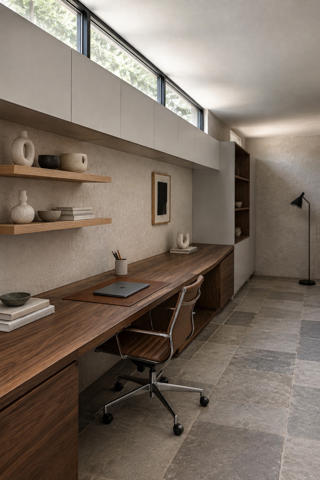 Modern minimalist office with long wooden desk, leather chair, and floating shelves.
