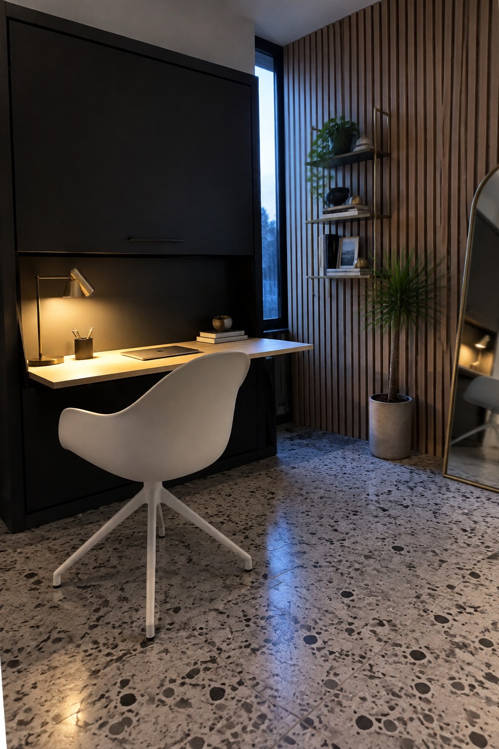 A recessed light wood desk sits under dark cabinetry with a white swivel chair, terrazzo floor, and wood slat wall with floating shelves.
