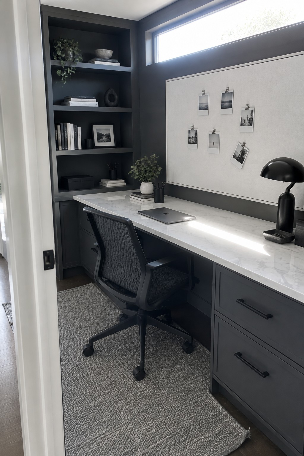 A compact home office with dark built-in shelves and drawers, a white marble desk surface, a black mesh office chair, and a large whiteboard above the desk.