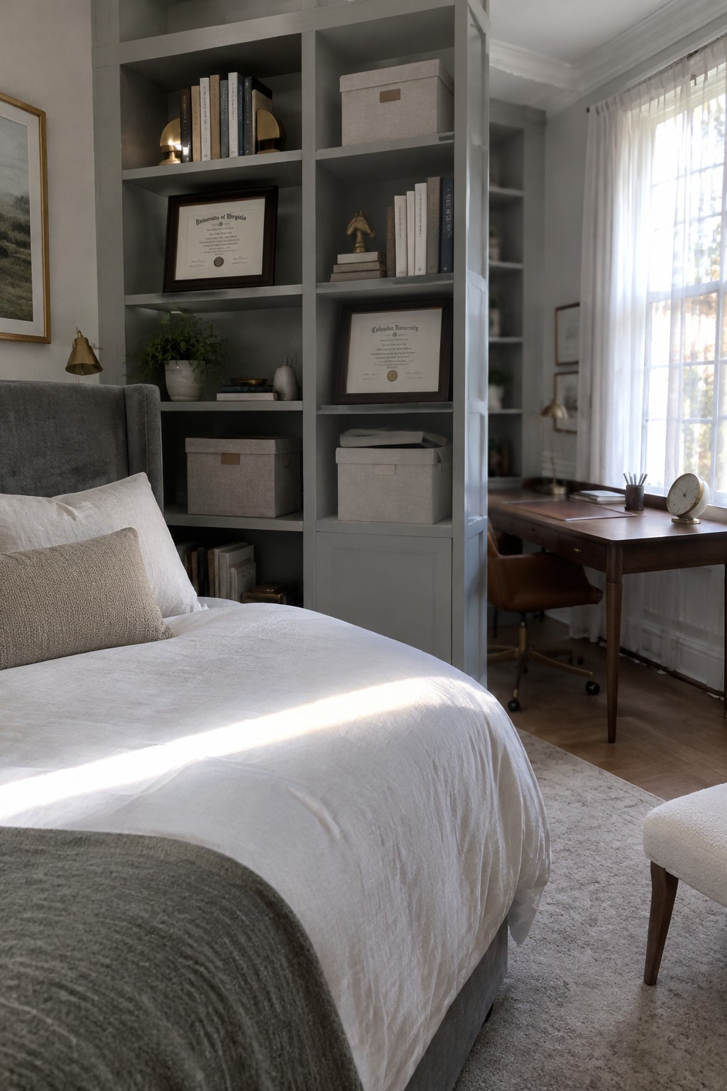 Cozy bedroom with gray bookshelves holding diplomas, white bed, wooden desk, and sunlit window