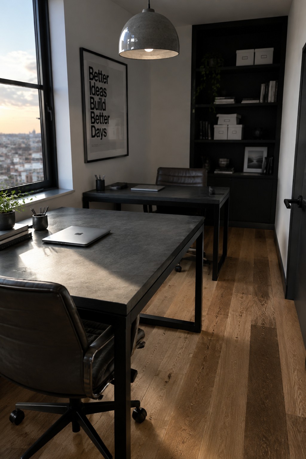 A home office with two dark desks and brown leather office chairs on wood flooring, a large window on the left, a framed poster on the wall, and black built-in shelves in the background.