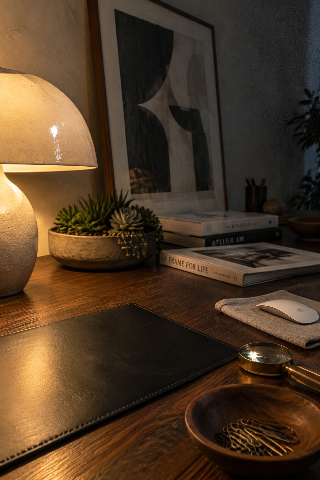 Wooden desk with lit lamp, succulents, books, mouse, magnifying glass, and clips.