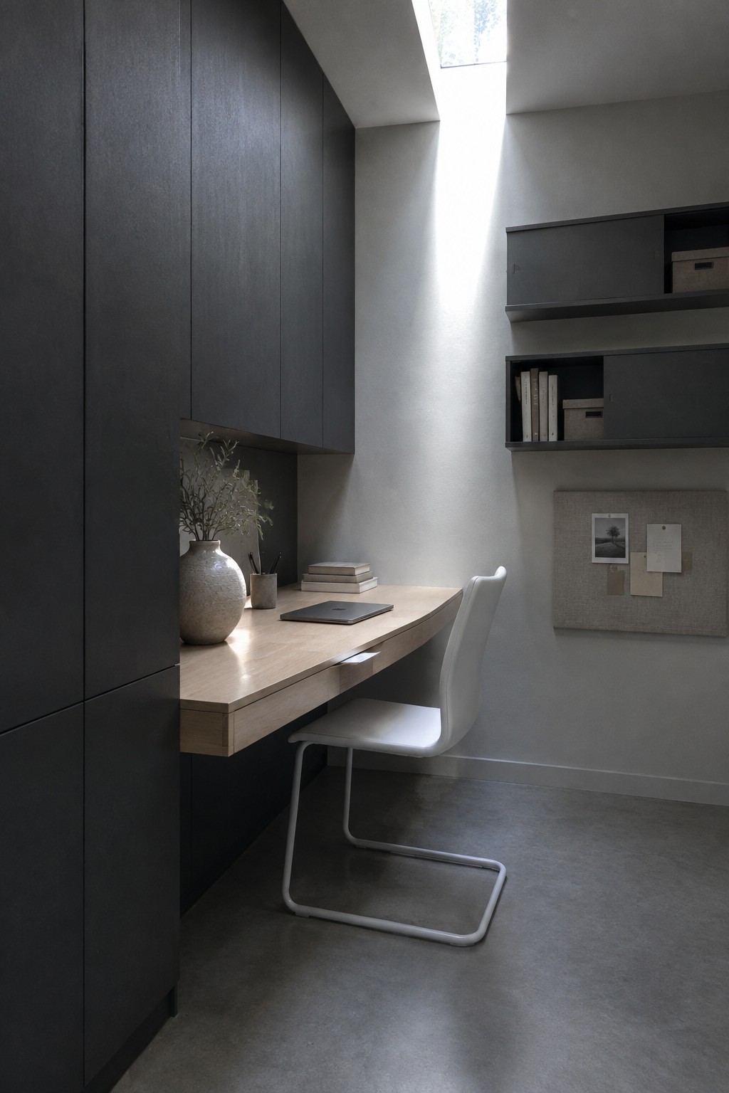 Minimalist wooden desk with white chair beneath skylight in dark cabinet nook